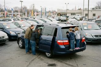 Famille nombreuse avec trois enfants inspectant un monospace 7 places d'occasion chez un concessionnaire de véhicules d'occasion